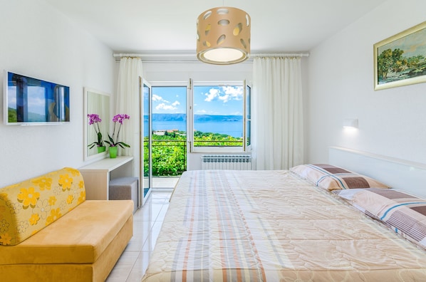 A hotel room with a bed, a sofa, a TV, and a view of the sea.