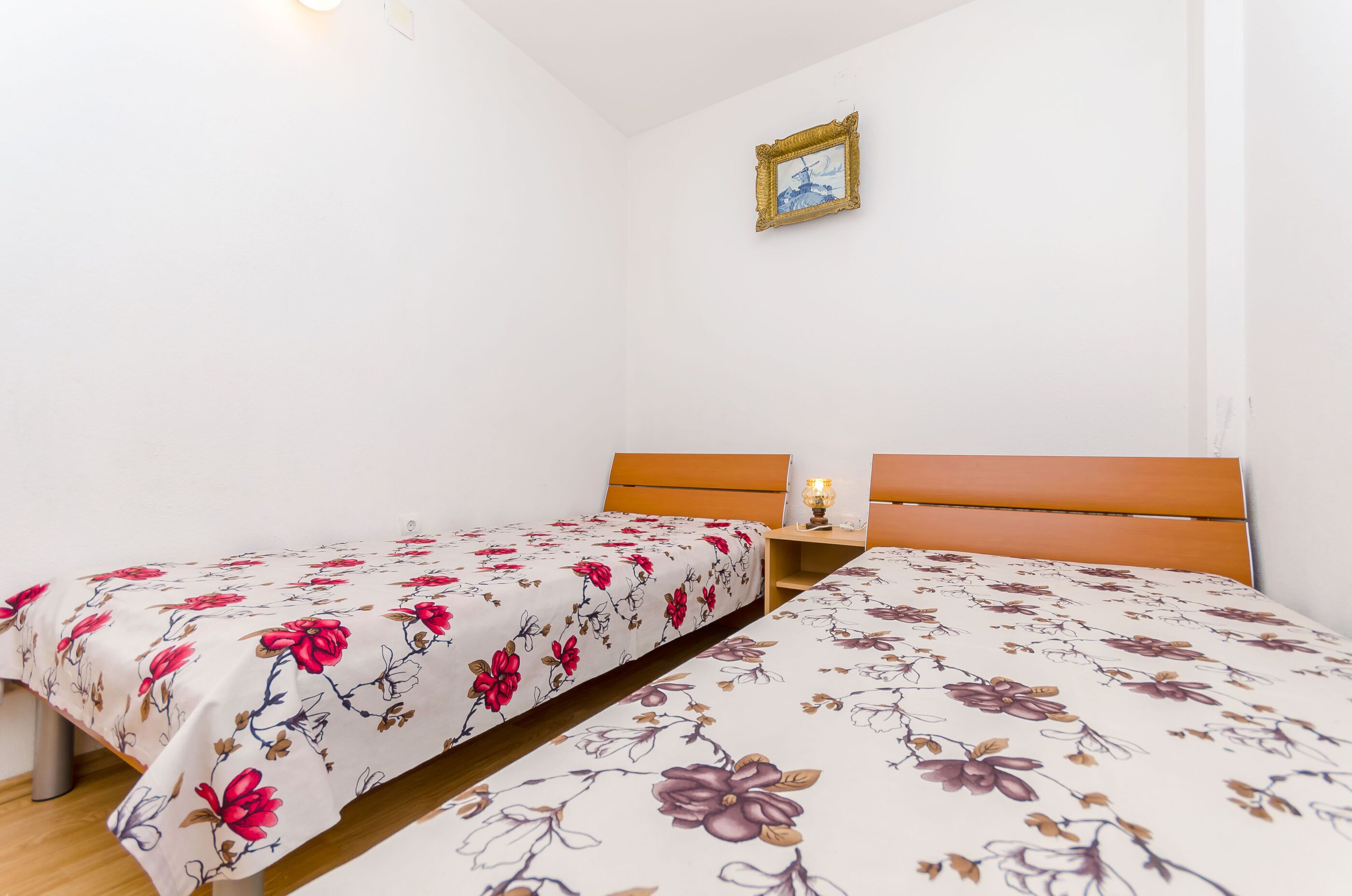 A bedroom with two single beds, a nightstand, and a framed picture on the wall.