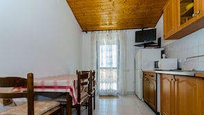 A compact kitchen with wooden cabinets, a dining table with chairs, a television, and a window with curtains. - Apartments Kursan (Okrug Gornji)
