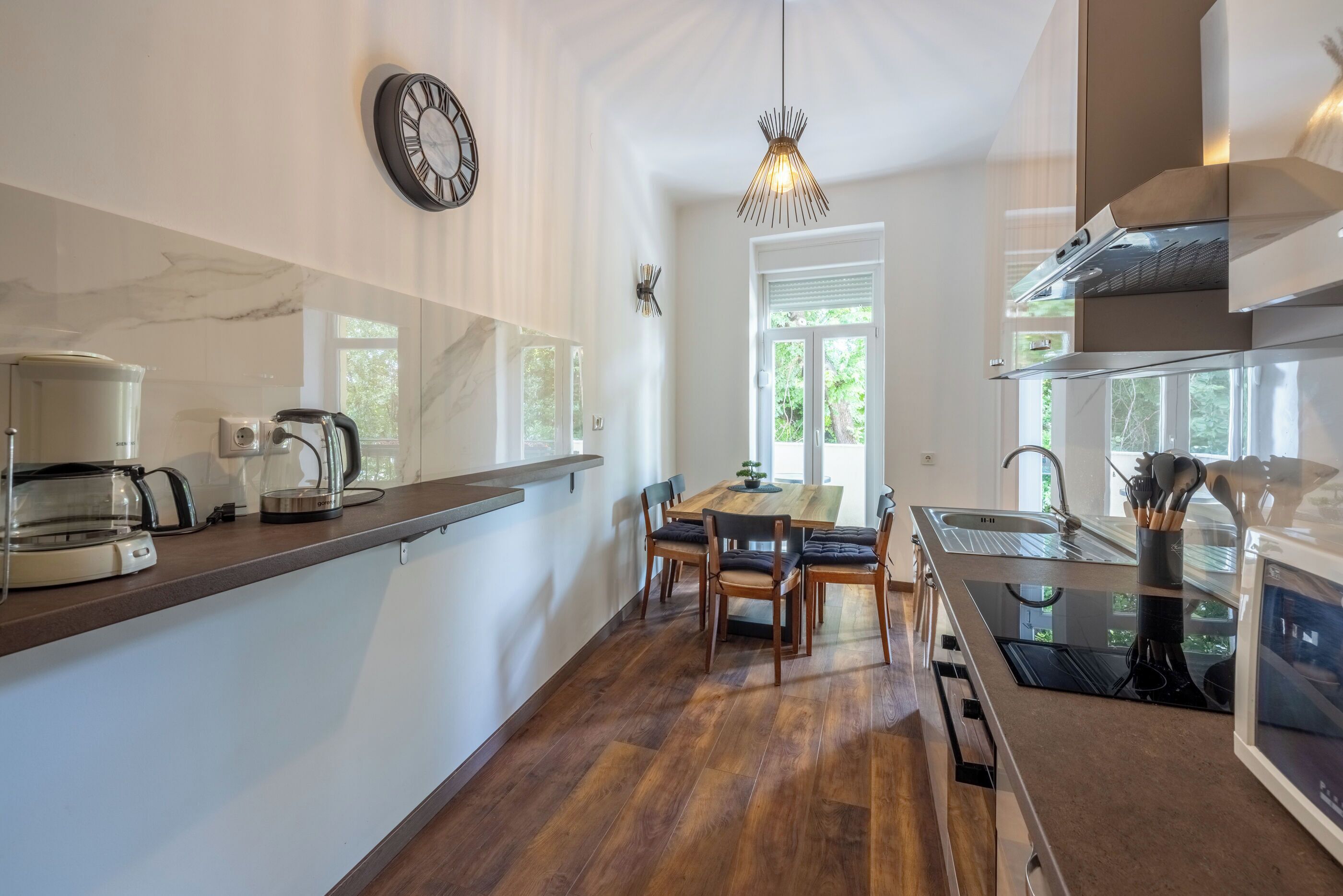 A modern kitchen with a marble countertop, a built-in oven, and a dining area with a table and chairs.