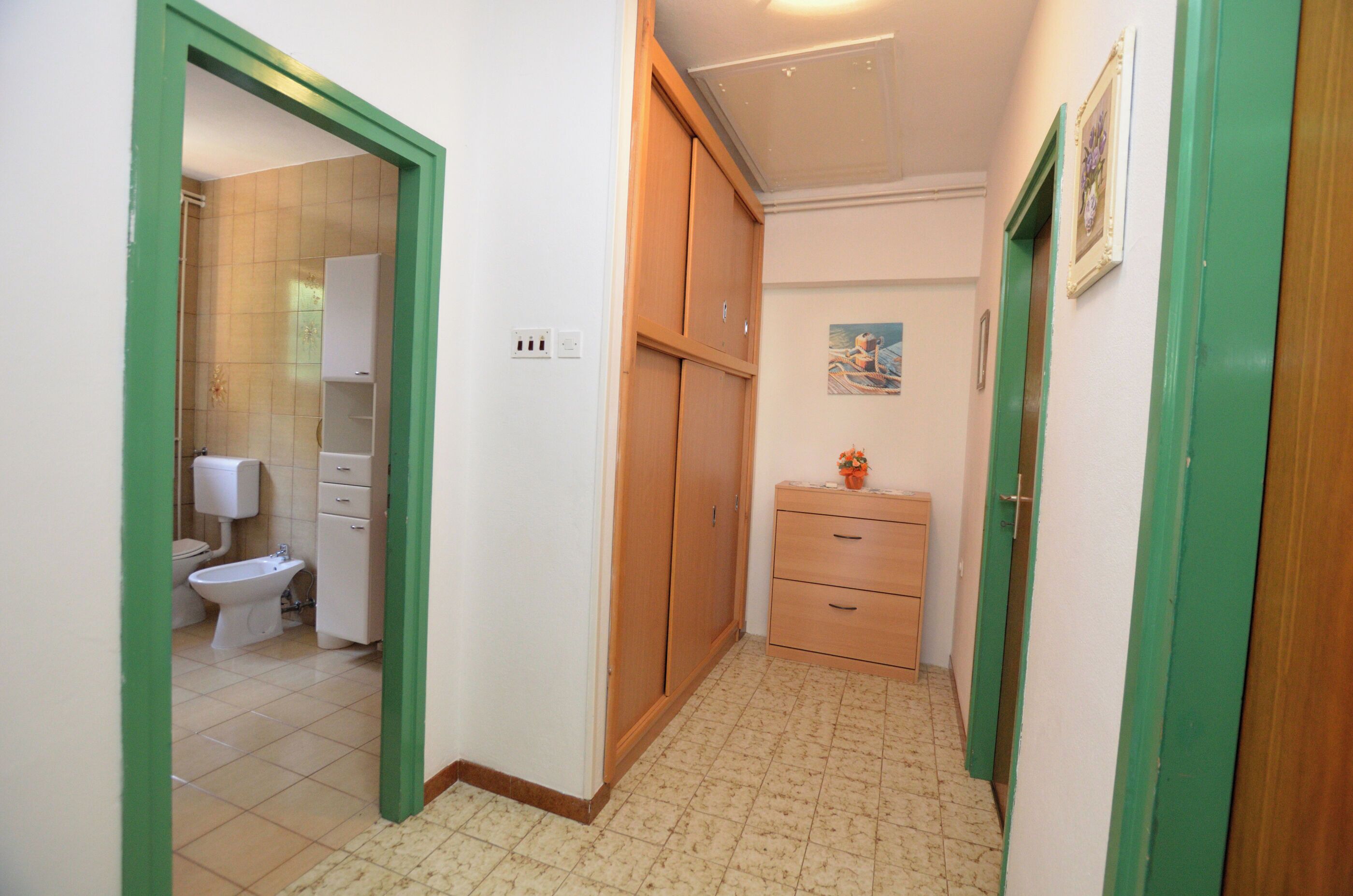 A narrow hallway with a wooden wardrobe, a small cabinet, and a toilet visible in the adjacent room.