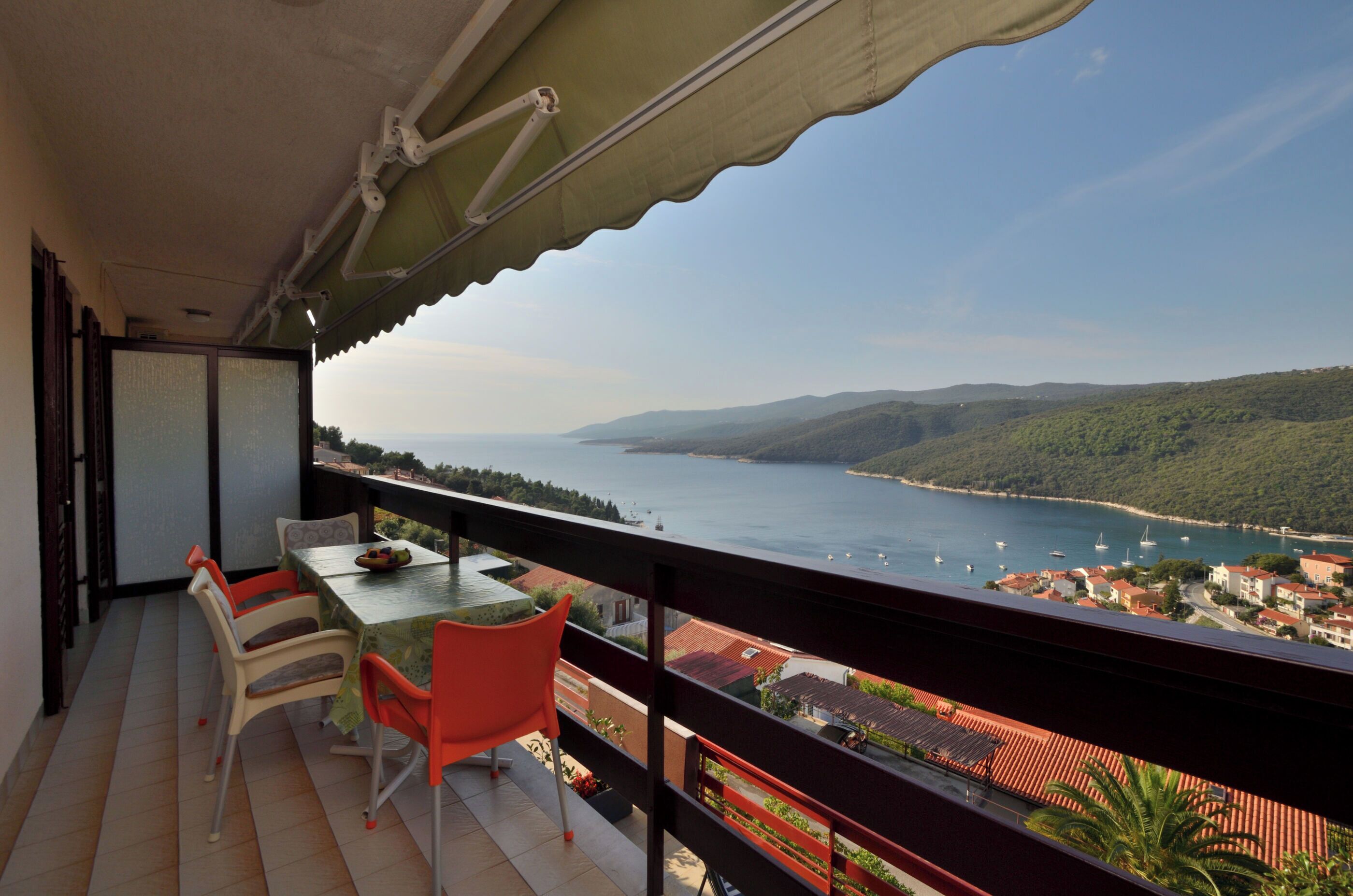 Un balcone con tavolo e sedie, vista su una cittadina costiera e il mare.