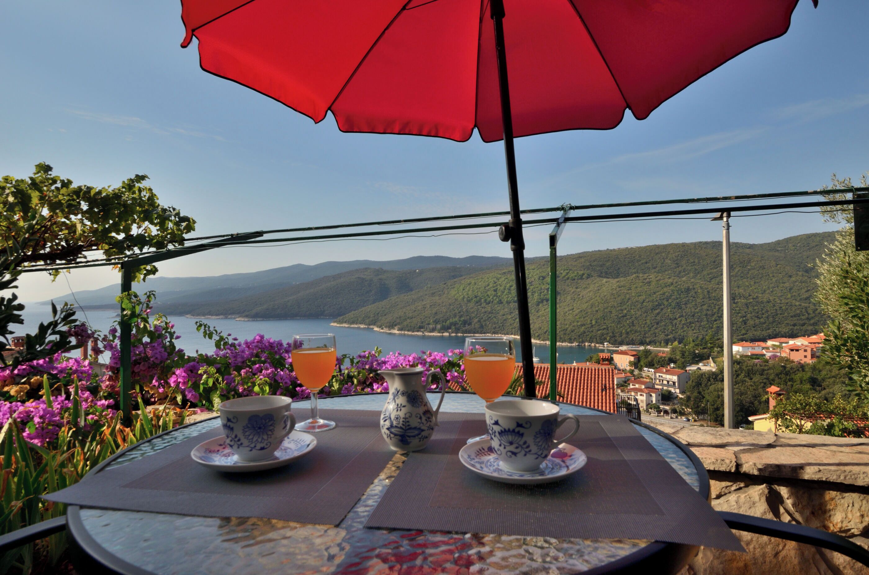 Une table avec deux tasses et un pichet, placée devant un paysage pittoresque comprenant un lac et des montagnes.