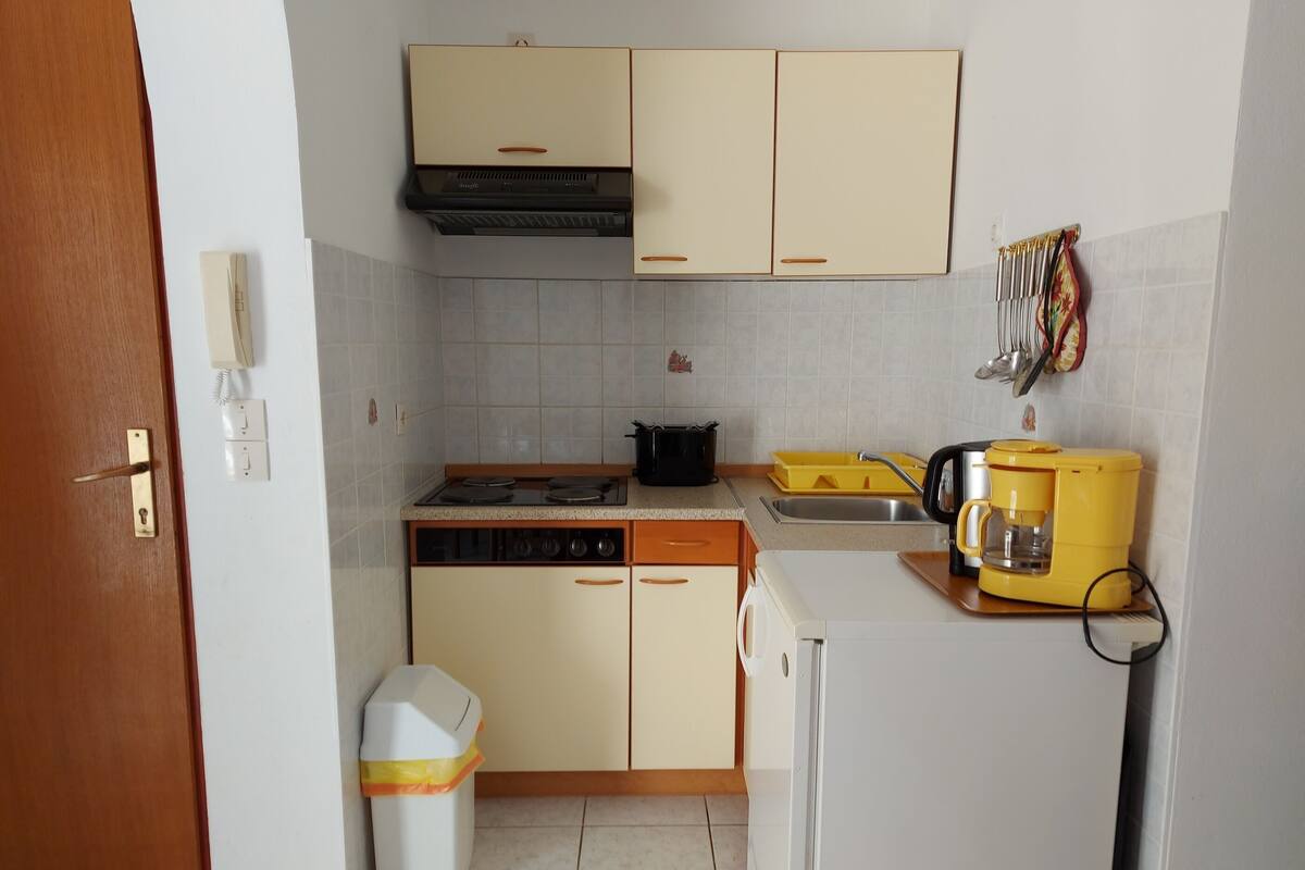 Una cocina compacta con estufa, lavamanos y cafetera.