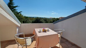 A balcony with a table and chairs, a tablecloth, and a view of trees and houses. - Villa Pave (Jadranovo)