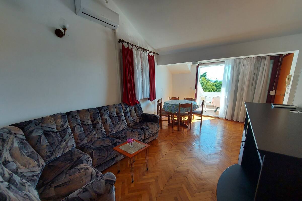 Una sala de estar con un sofá estampado, una mesita, un comedor con sillas y un televisor.