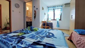 Un dormitorio con una cama, una silla, una mesa con botellas, una ventana con cortinas y un armario.