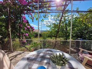 A patio with a checkered table, a cactus plant, and a pergola with pink flowers. - Rooms Anchy (Crikvenica)