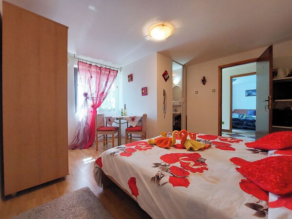 A bedroom with a bed, a desk, and a chair. There is a door leading to another room. - Rooms Anchy (Crikvenica)