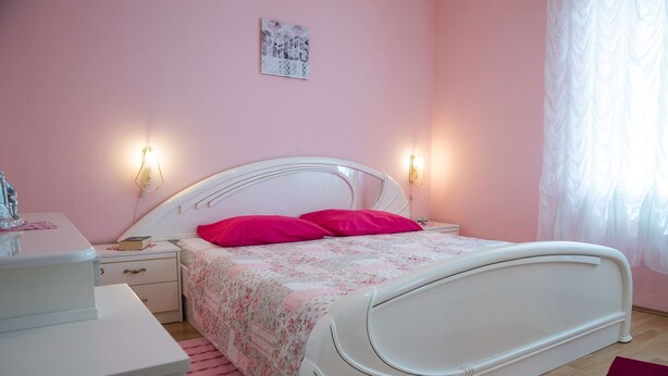 Une chambre à coucher avec un lit blanc, des murs roses et deux lampes de chevet.