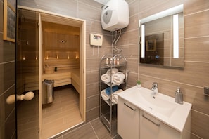 A modern bathroom with a wooden sauna, a wall-mounted heater, a towel rack, and a sink with a mirror. - House Denis (Crikvenica)