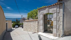 A narrow street with stone walls and a tiled roof, leading to a building with a stone facade and an archway entrance. - House Denis (Crikvenica)