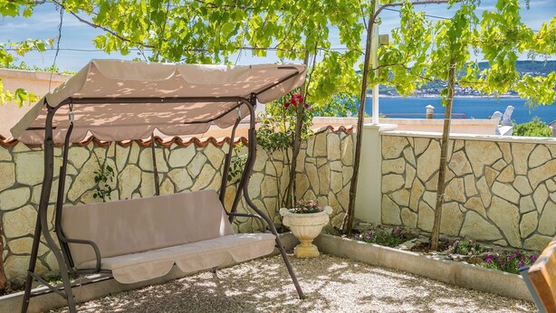 A patio with a swing seat, a potted plant, and a view of the sea. - House Denis (Crikvenica)