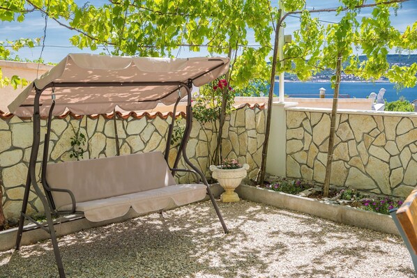 A patio with a swing seat, a potted plant, and a view of the sea. - House Denis (Crikvenica)