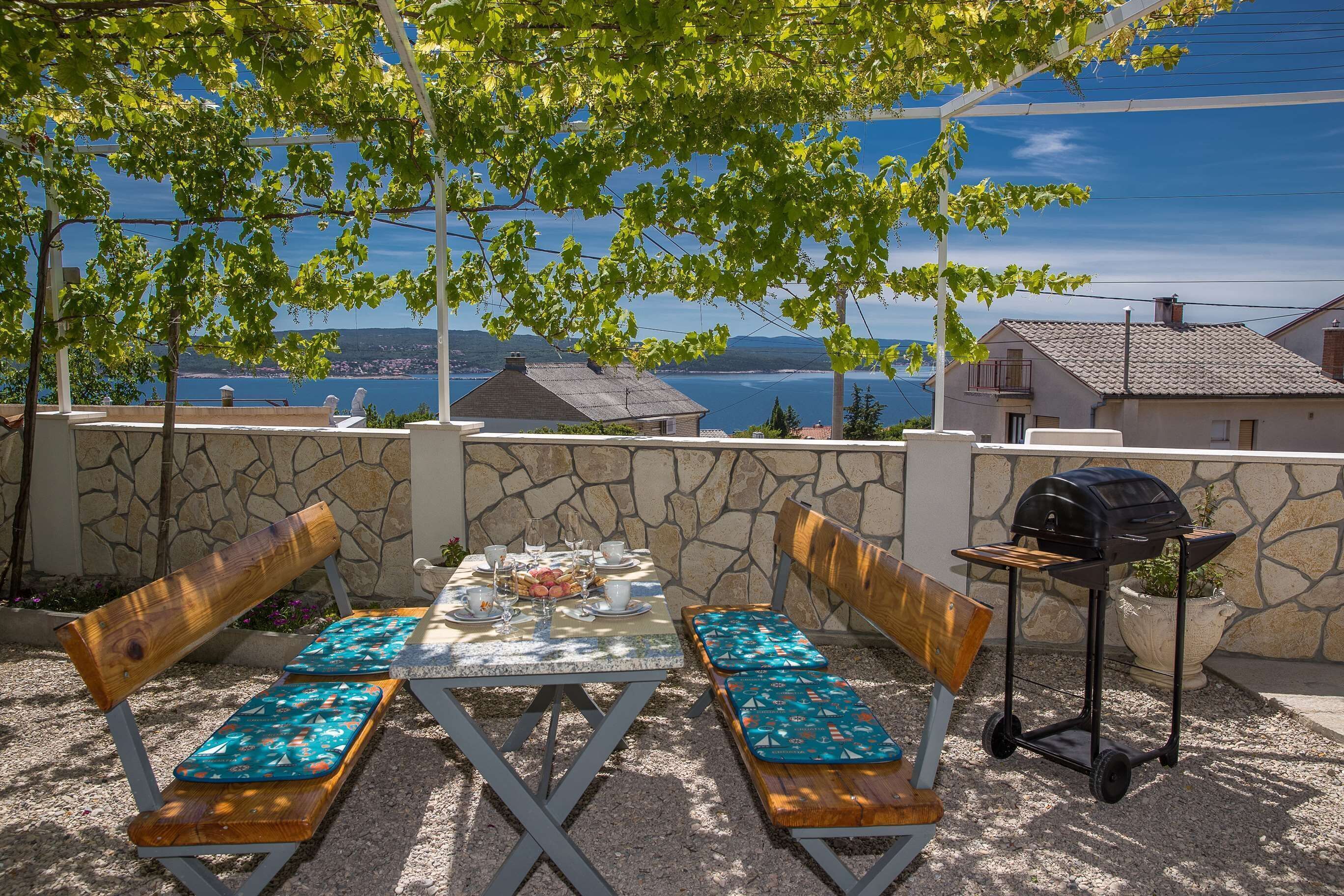 An outdoor patio with a table set for dining, benches, and a grill.