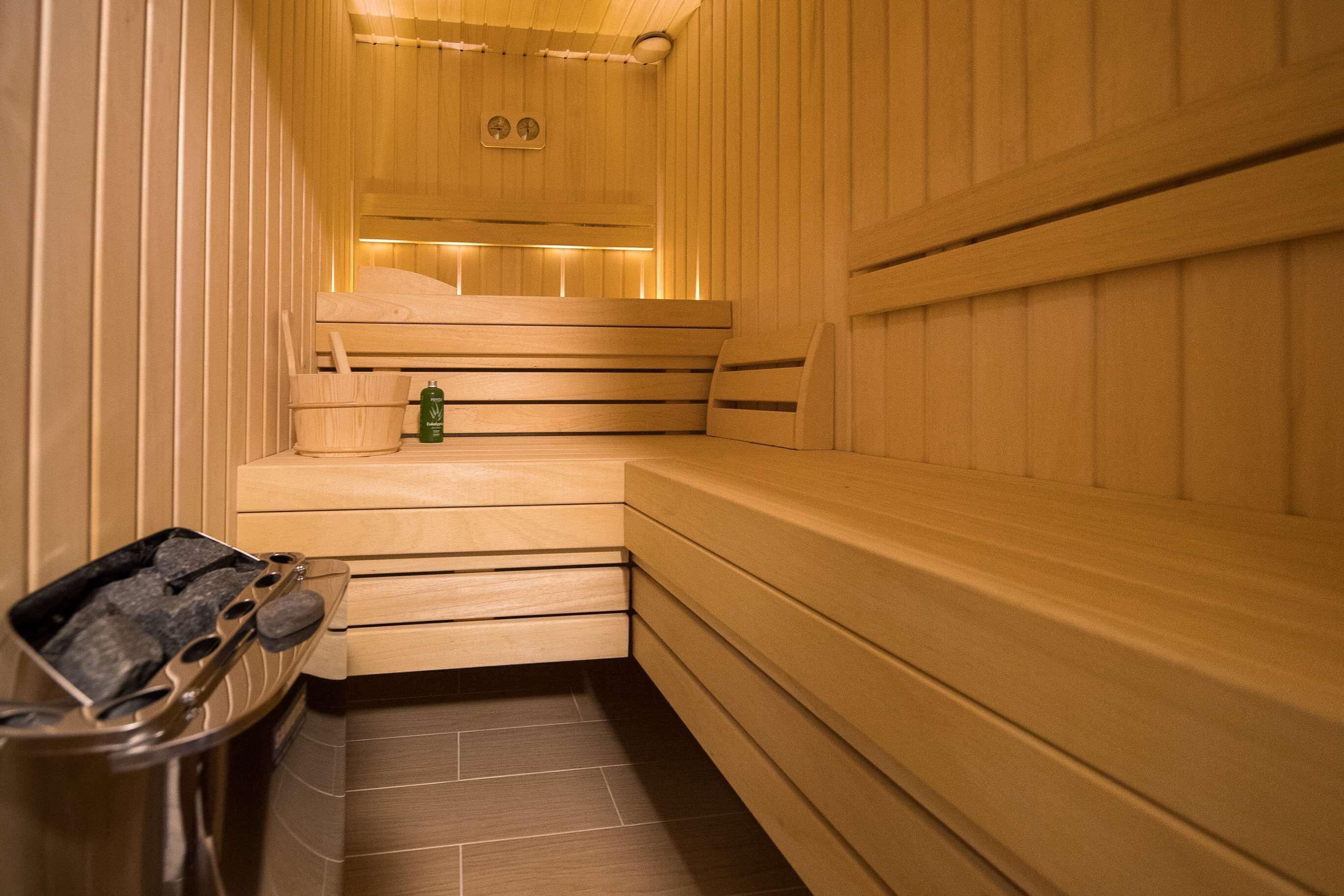 A sauna room with wooden benches, a bench heater, and a bottle of oil.