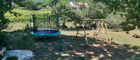 A backyard with a trampoline, swing set, and stone wall.