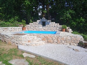 Zwembad met stenen muren en een kleine waterval, omringd door grind en groen.