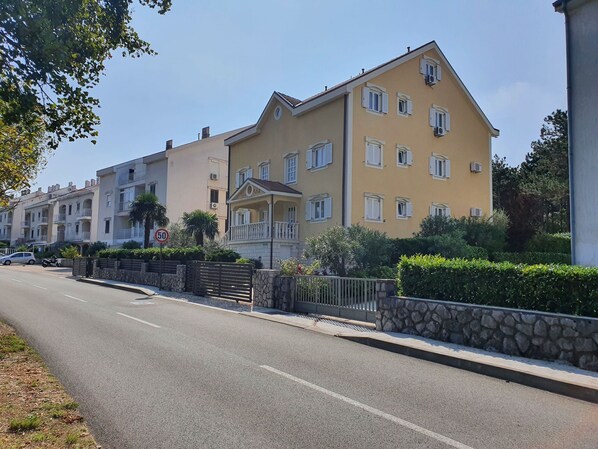 A row of yellow buildings with balconies, a stone wall, and a clear sky. - Apartments Villa Anne (Jadranovo)