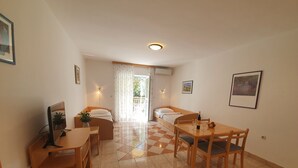 Una stanza compatta con un letto, una scrivania e un tavolo da pranzo. Si vede una finestra con tende, una luce a soffitto e un quadro appeso al muro.