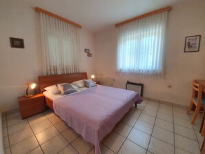 A bedroom with a bed, two bedside tables, a nightstand, a radiator, and a chair.