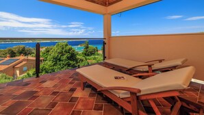Ein überdachter Außenbereich mit zwei Liegestühlen und Blick aufs Meer.