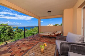 A balcony with a view of the sea, a wicker sofa, a table with a vase, and a chair. - House Davorka (Supetarska Draga)