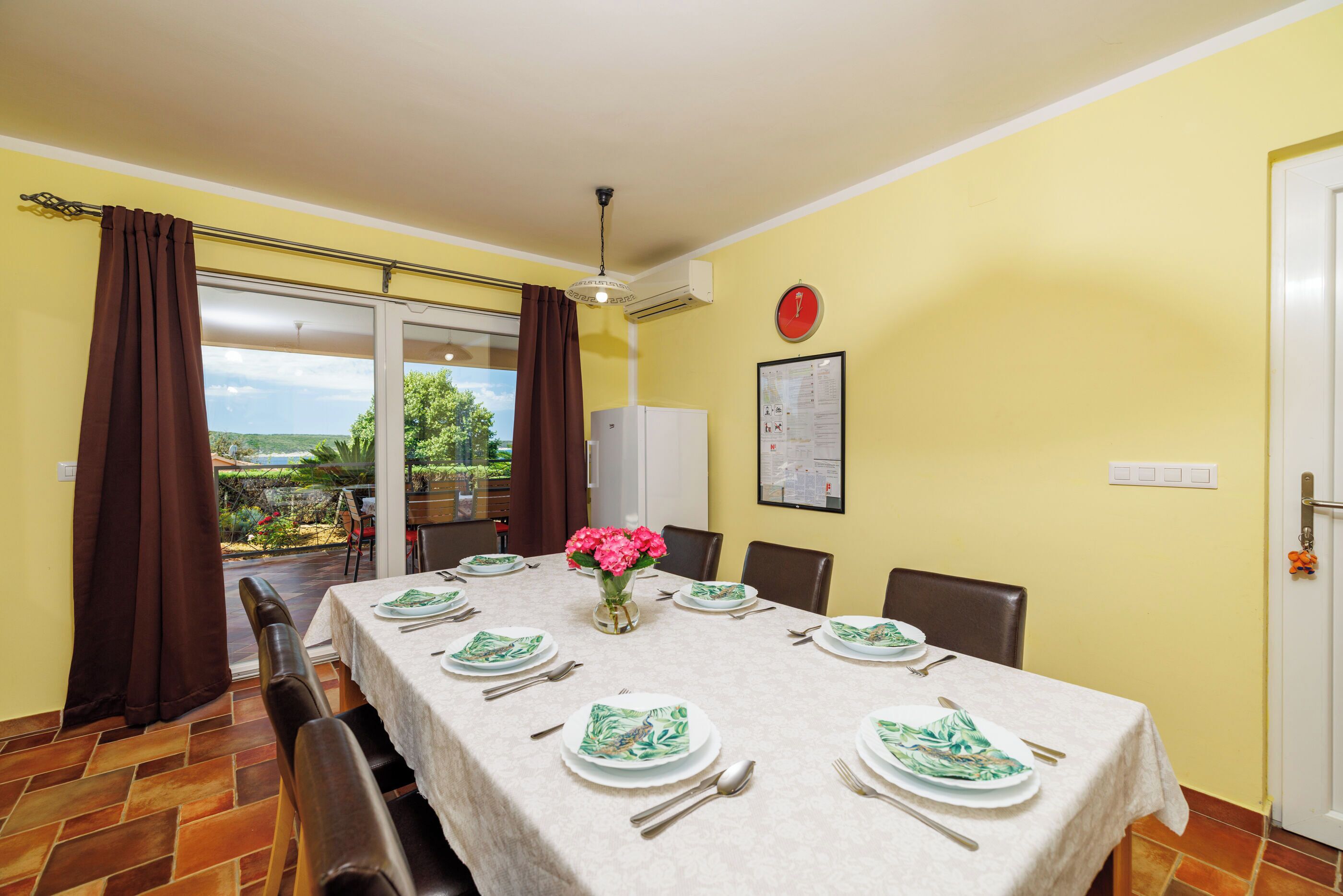 Comedor con una mesa dispuesta para cuatro personas, un jarrón de flores y vistas a zonas verdes al exterior.