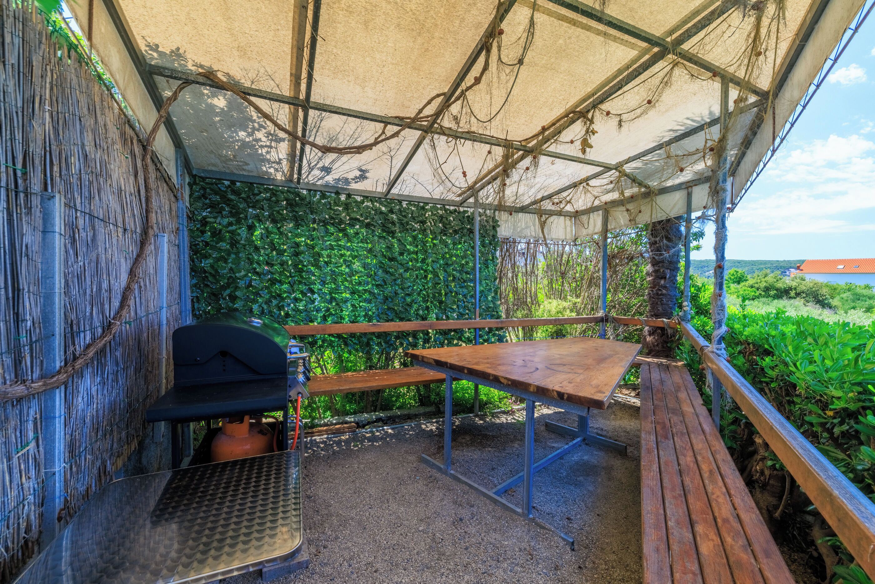 A covered outdoor area with a grill, a table, and benches.