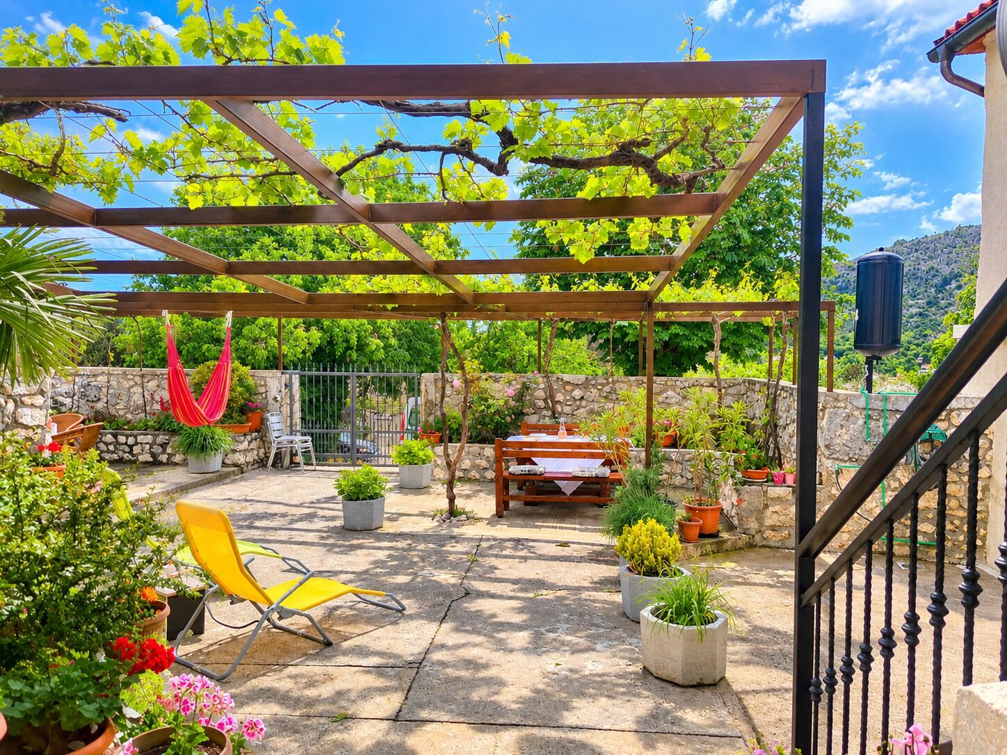 A covered outdoor patio with a pergola, seating, and potted plants.