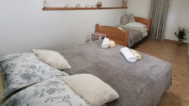 Quarto com duas camas, uma cabeceira de madeira, uma prateleira com objetos decorativos e uma janela com cortinas.