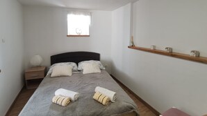 Quarto com cama, mesas de cabeceira, janela decorada com um coração e uma estante com objetos.