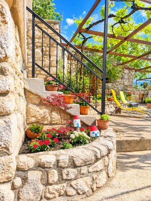 A stone building with a staircase leading to a covered outdoor area with potted plants and a seating area. - Apartment Maja (Bribir)
