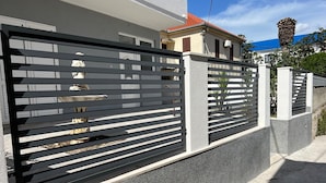 A modern building with a grey facade, a black metal fence, and a red-tiled roof. - Apartments Milica (Kastel Stari)