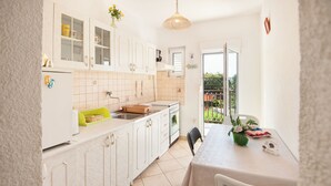 A kitchen with white cabinets, a dining table, and a view of the outdoors. - Apartments Milica (Kastel Stari)