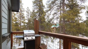 Un balcon équipé d’un barbecue et d’une bouteille de propane, donnant sur une zone boisée et offrant une vue sur un lac.