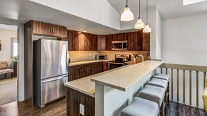 Une cuisine moderne dotée d’un îlot central, d’appareils électroménagers en acier inoxydable et de meubles de rangement en bois.