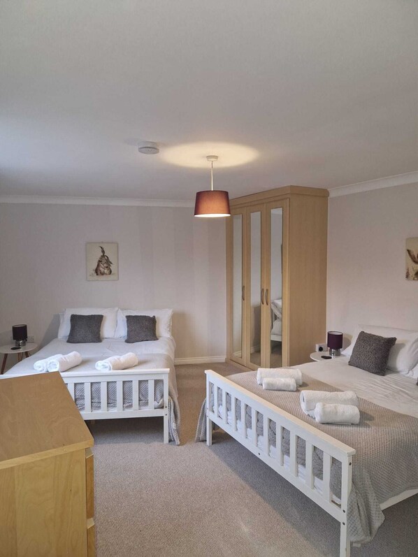 A bedroom with two beds, a wooden wardrobe, and a hanging light fixture.