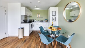 A modern kitchen with white cabinets, a dining area with a glass table and blue chairs, and a wooden floor.