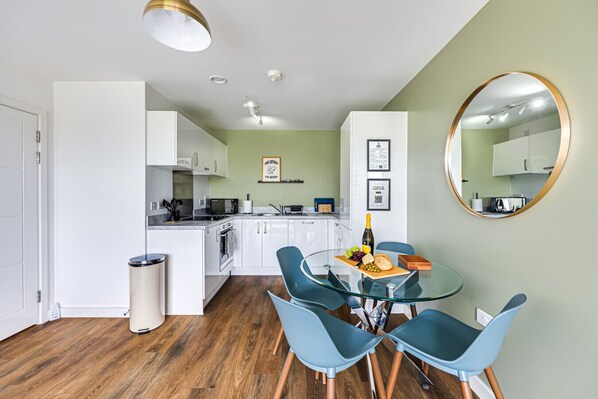 A modern kitchen with white cabinets, a dining area with a glass table and blue chairs, and a wooden floor.