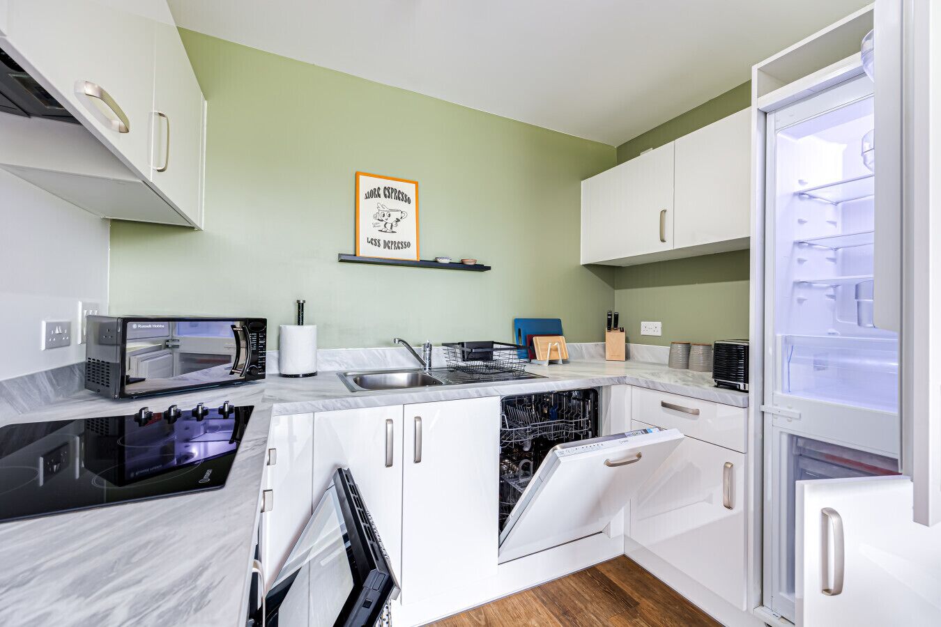 A modern kitchen with white cabinets, a built-in oven, a dishwasher, and a microwave.