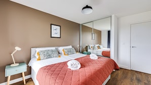 A modern bedroom with a large bed, a bedside table with a lamp, a mirror, and a door.