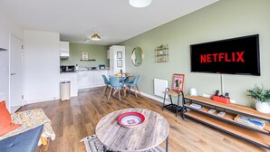 A modern living room with a round coffee table, a TV mounted on the wall, and a dining area with chairs and a table.