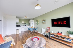 A modern living room with a round coffee table, a TV mounted on the wall, and a dining area with chairs and a table.