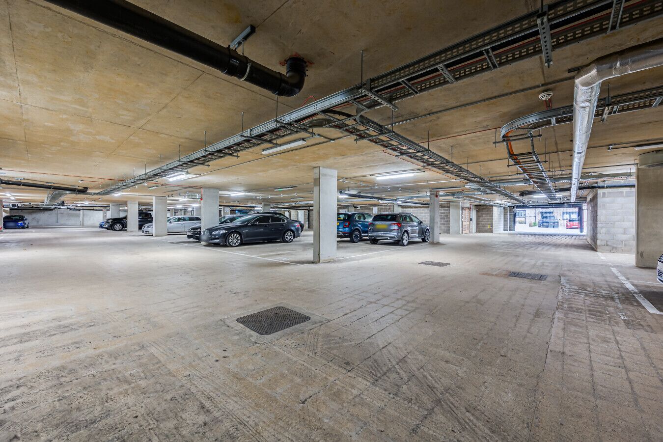 A multi-level underground parking garage with concrete pillars, metal beams, and ventilation ducts.