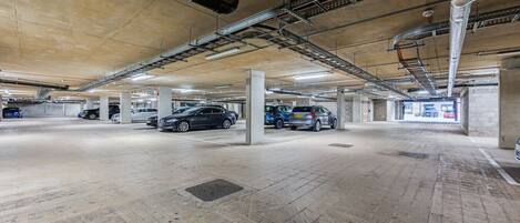 A multi-level underground parking garage with concrete pillars, metal beams, and ventilation ducts.