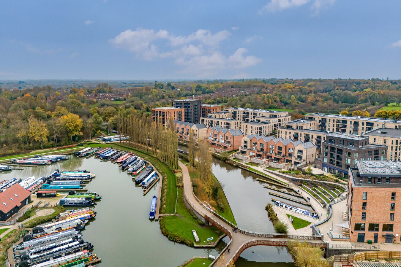 Zona residencial a orillas del río con modernos edificios de apartamentos, un puerto deportivo con barcos y un puente para peatones.