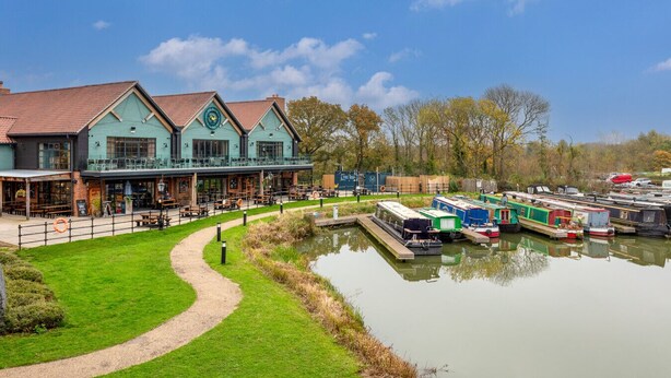 A riverside building with outdoor seating and a dock with boats.