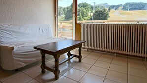 Et værelse med et træbord, en hvid sofa, et stort vindue med udsigt over landskabet og en radiator.