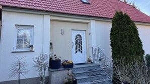 Ein Haus mit rotem Ziegeldach, einer weißen Tür mit dekorativem Glasfenster und einem kleinen Fenster links.